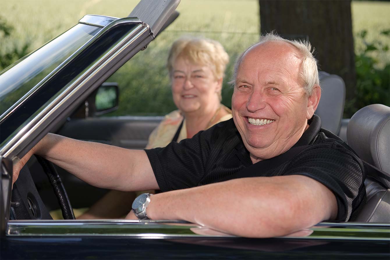 Smiling senior couple drive a black convertible on a sunny day