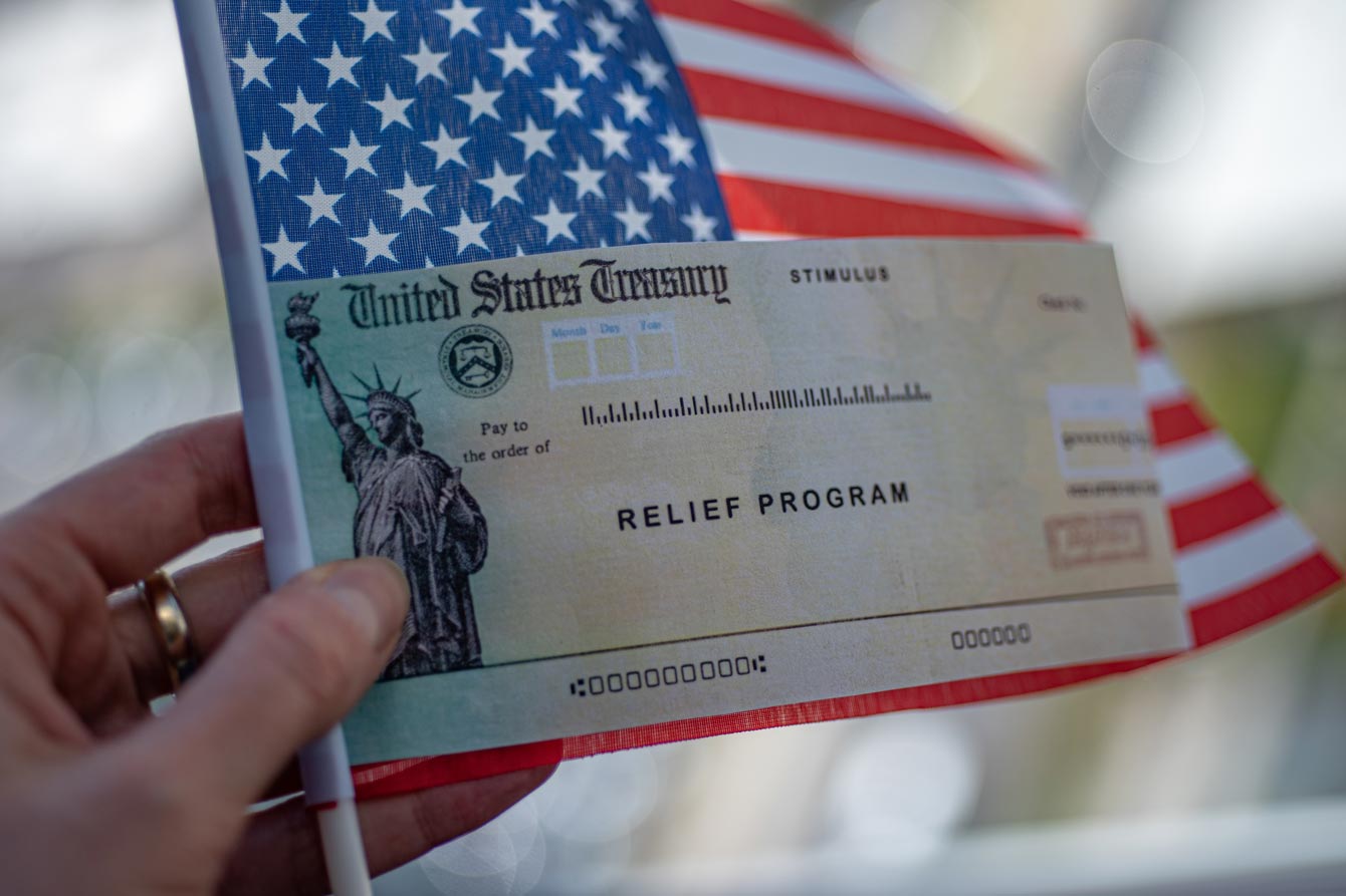 Hand holds a check from the US treasury with an American flag in the background
