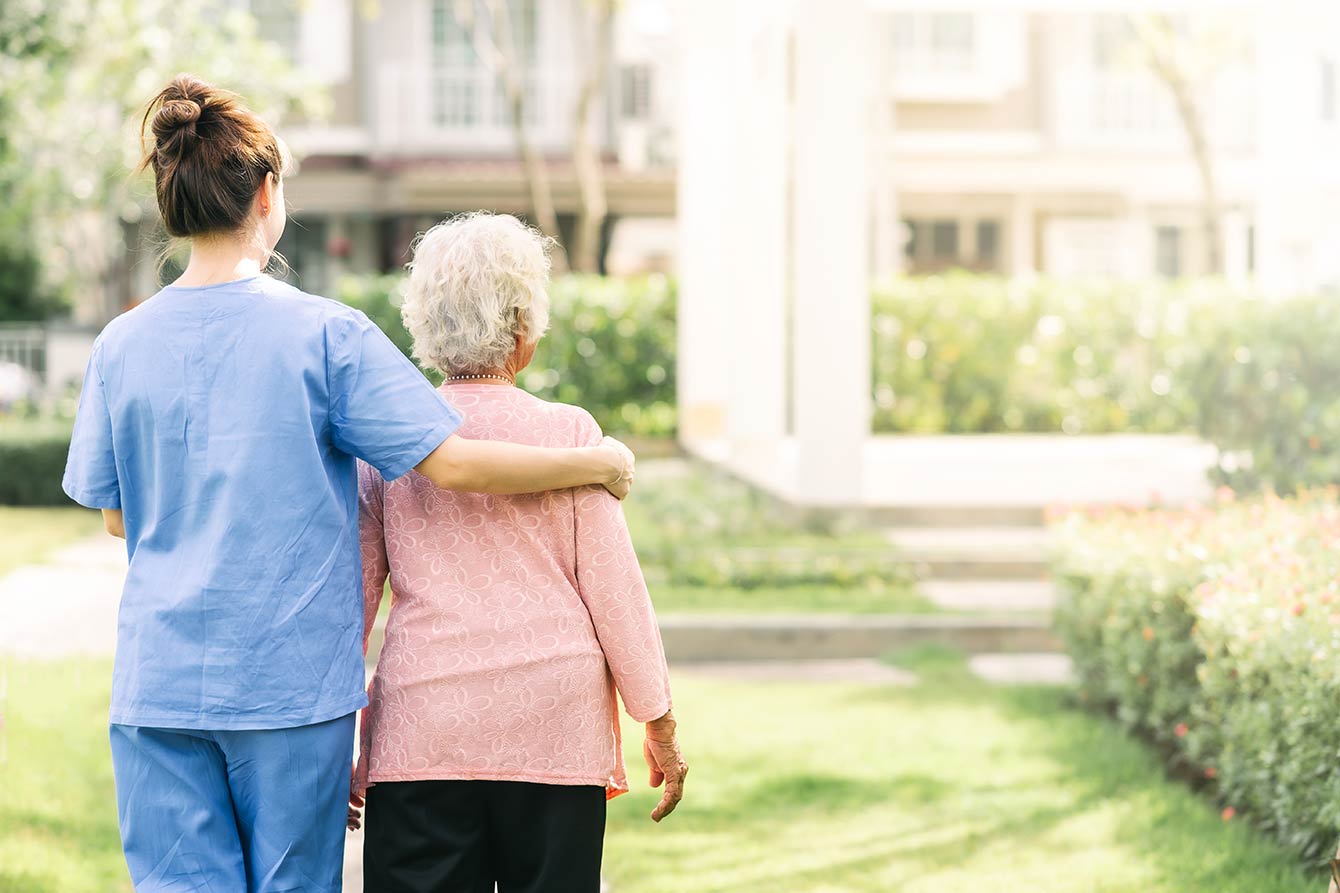 Nurse and senior woman standing outside nursing home