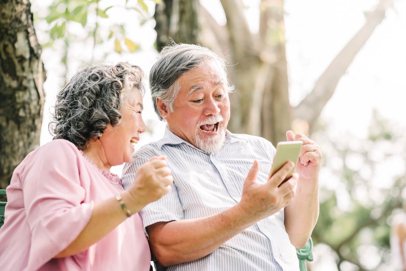 senior couple reading great news from their phone outdoors