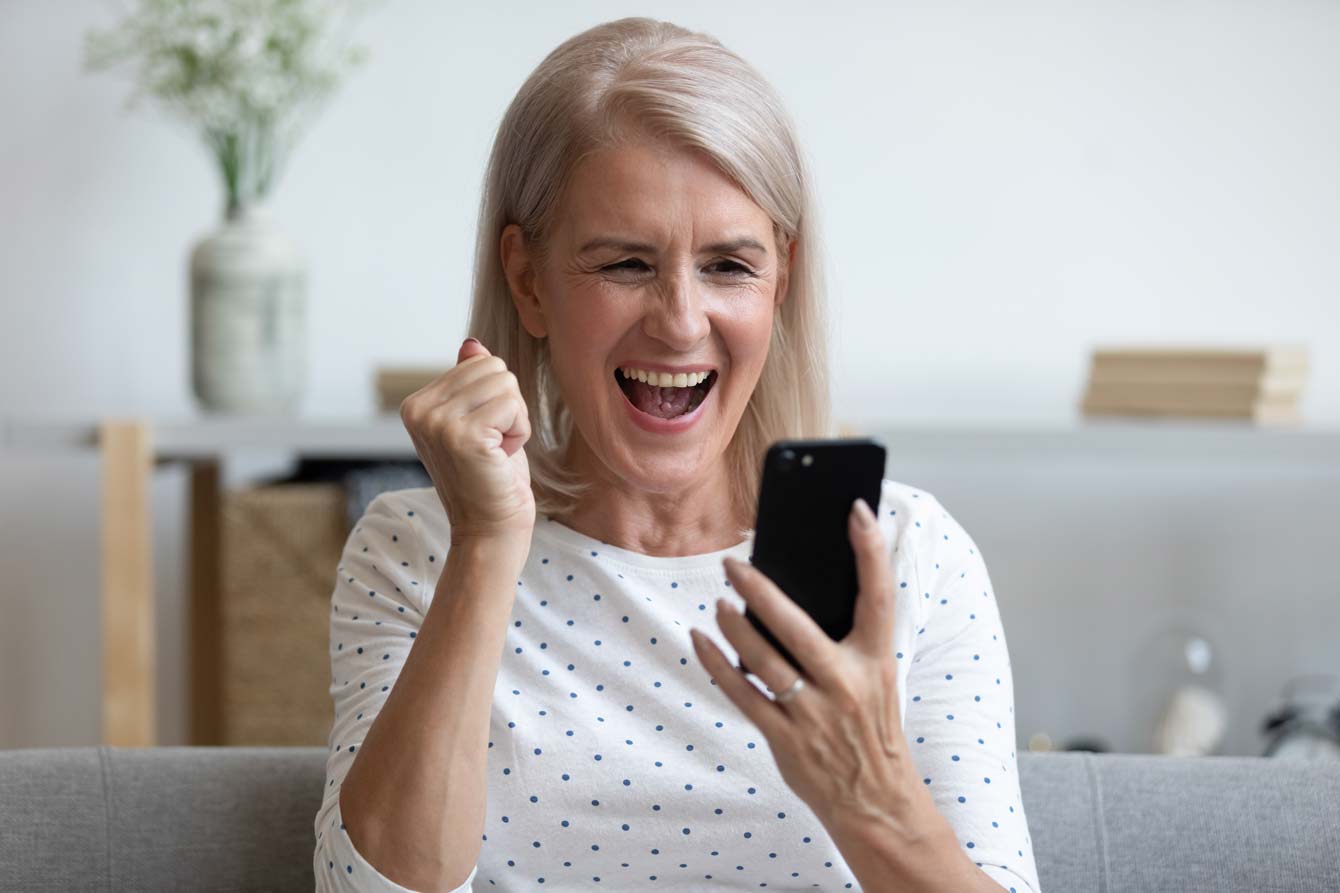 An excited senior female reacts to winning on her cell phone