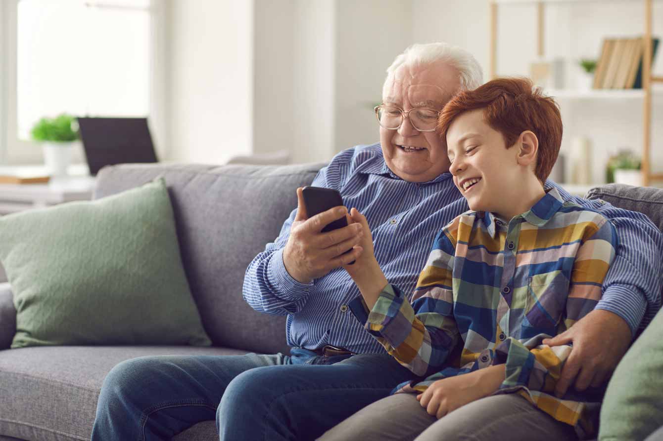 An elderly man plays a game with his grandson while sitting on couch