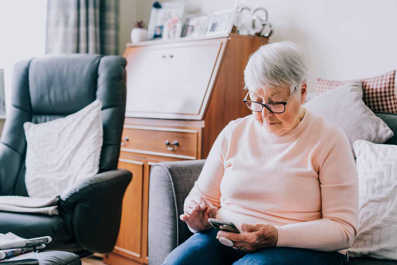 An older woman sits on her couch playing with her cell phone