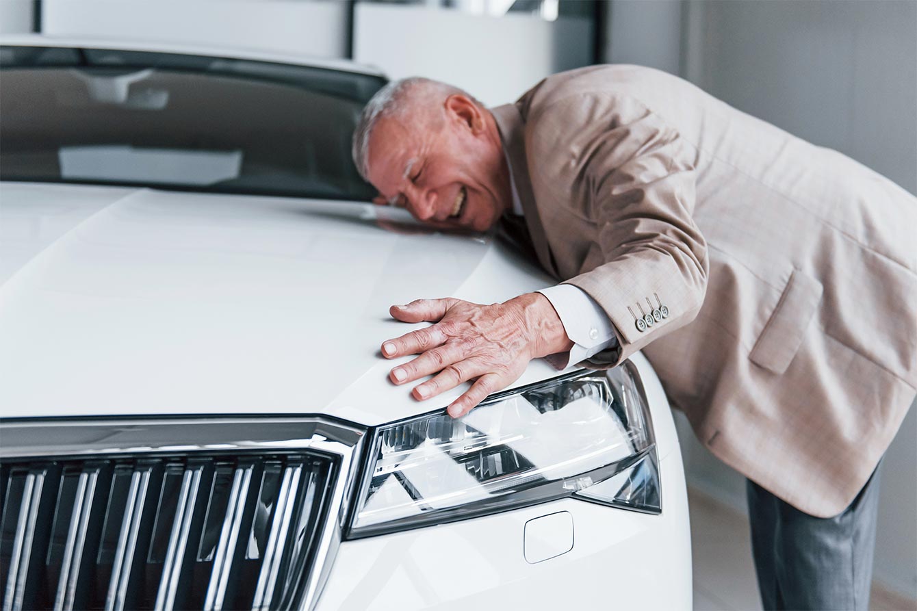 Cheerful older man in formal wear stands in front of modern white car