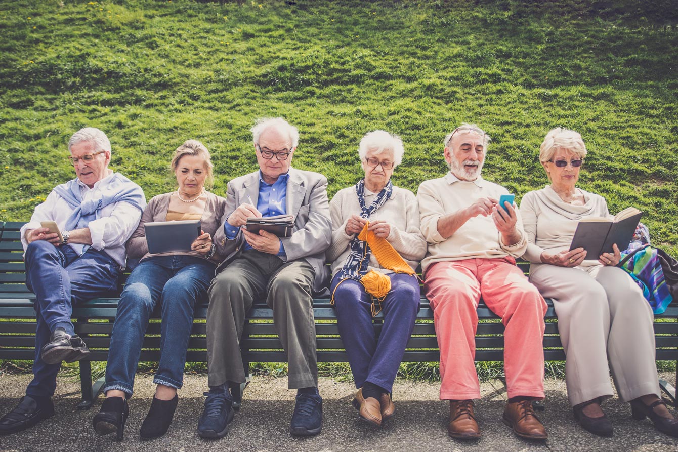 Row of seniors sitting on a bench with phones and tablets