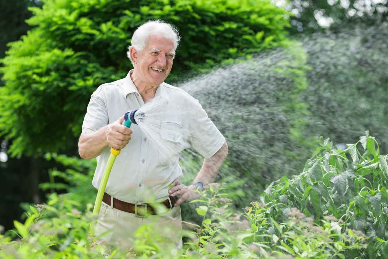 An older smiling man waters his lawn