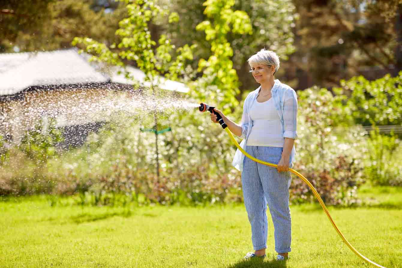 An older woman waters her lawn