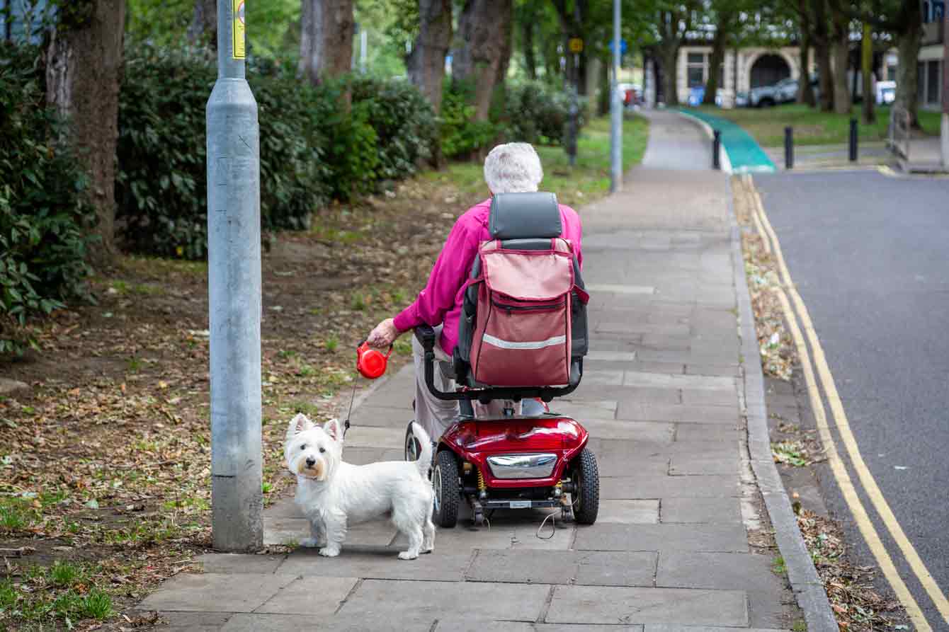 An elderly woman on a mobility scooter walking her dog