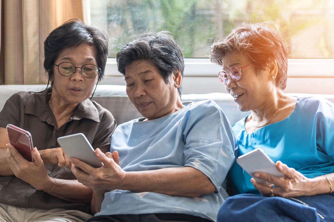 Three senior asian women sit on couch looking at smart phone
