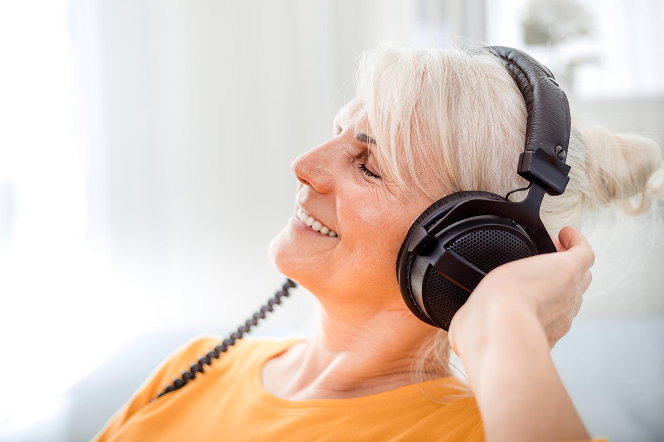 Relaxes senior woman listening to favorite podcast with big headphones