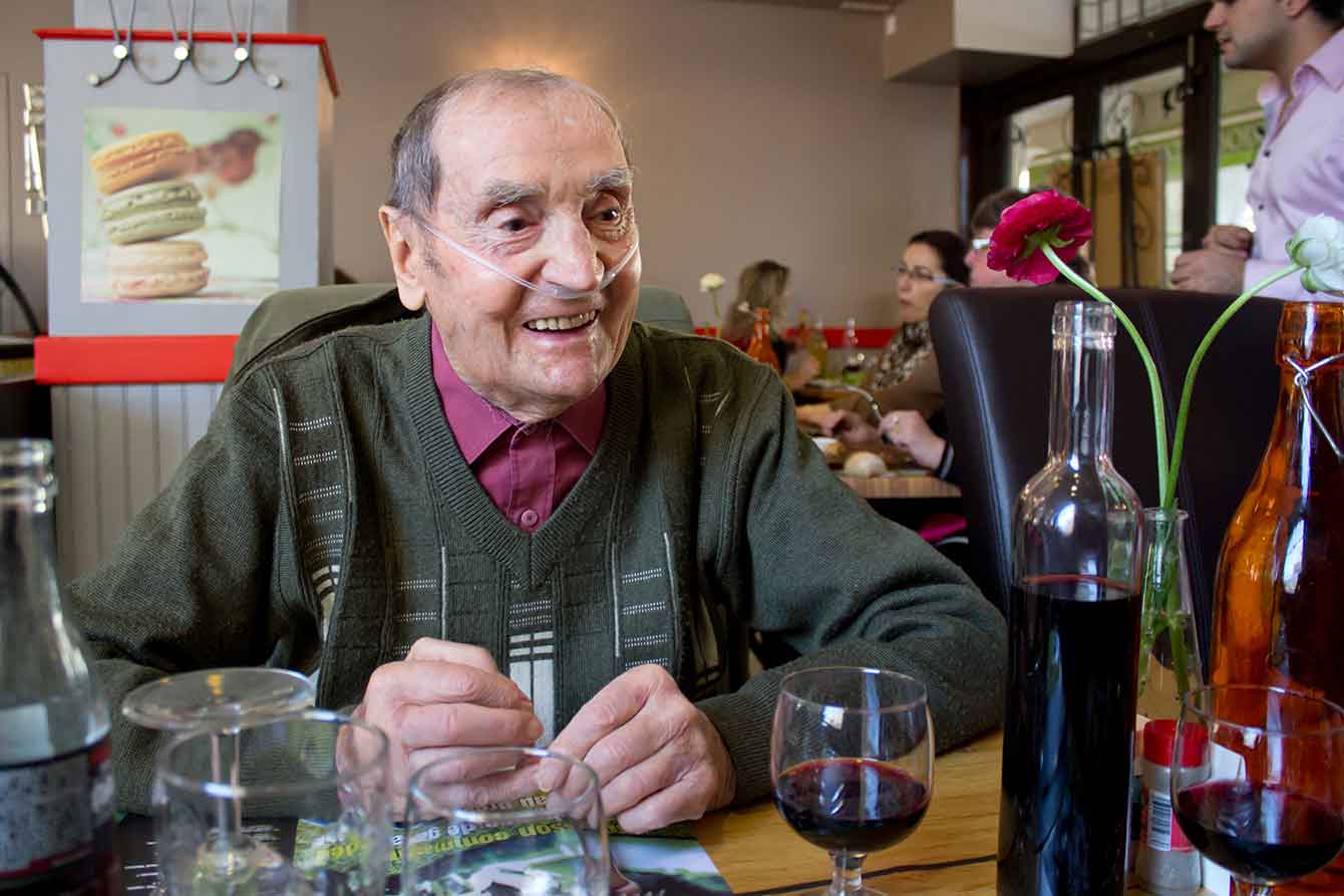 An older man sits happily in a restaurant with oxygen tubes in his nose