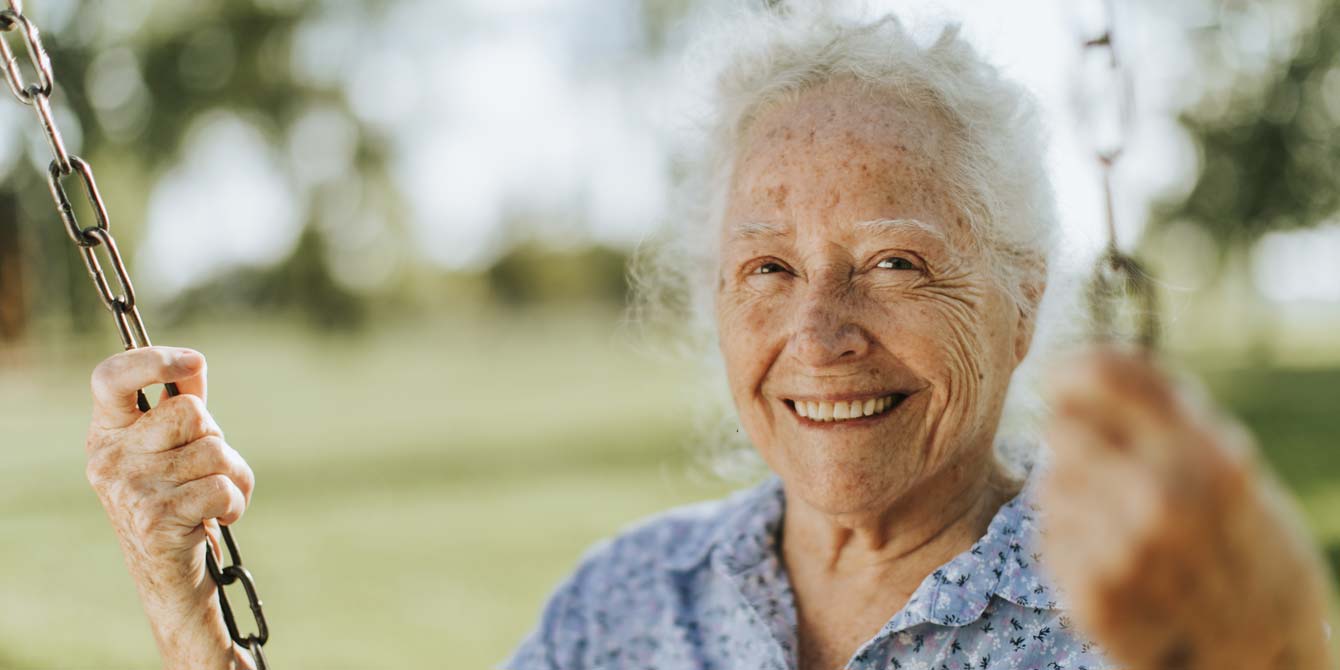 A cheerful senior woman on a swing at a park