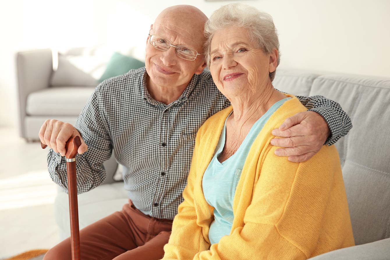 Elderly couple with cane sit on couch in living room