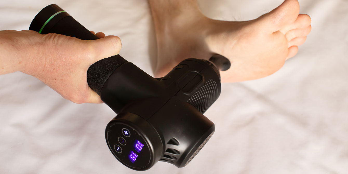Man massaging foot with massage percussion device after workout.