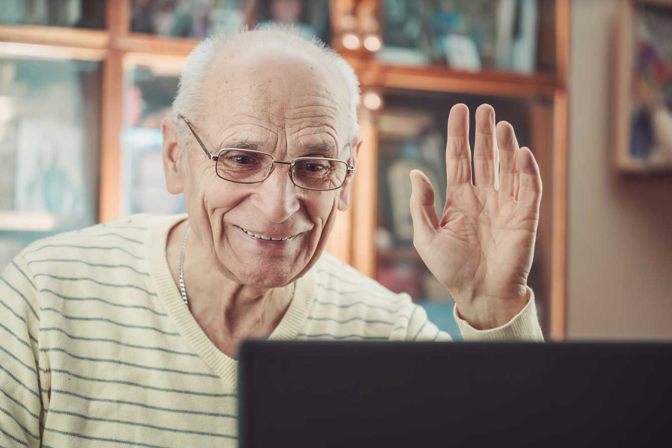 An older man waves to family on his laptop