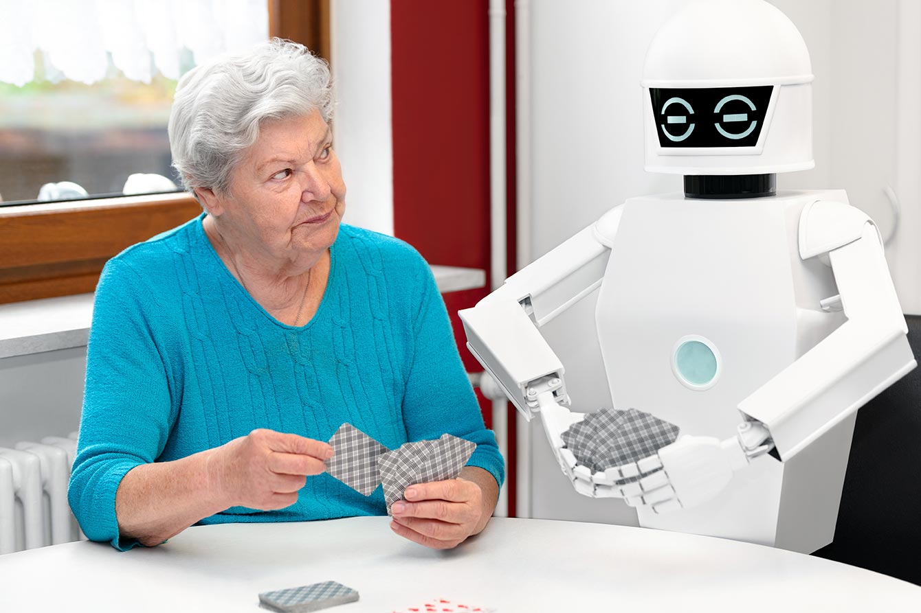 Senior woman plays cards at a table against a white robot