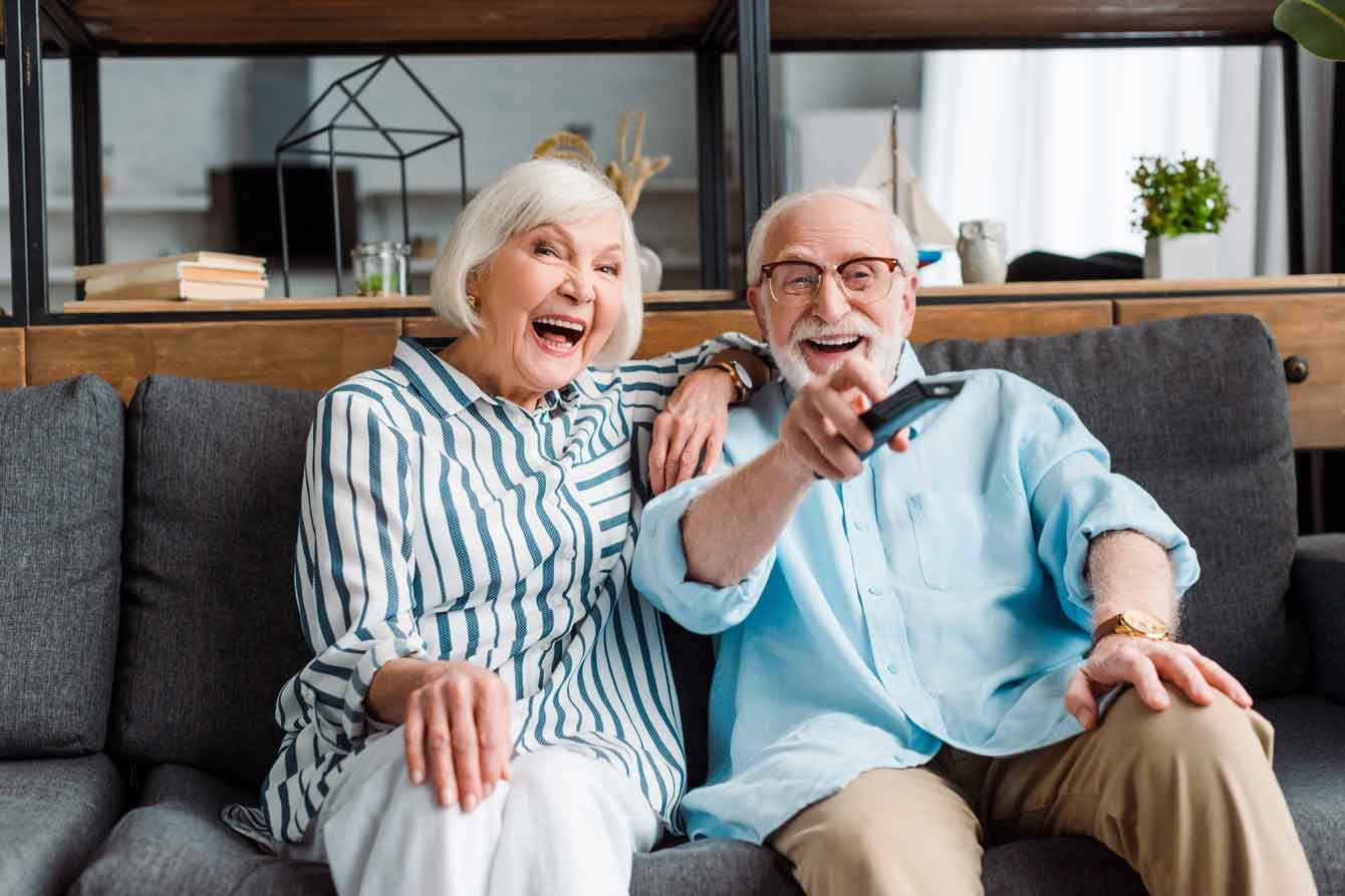 Senior couple laughing while watching TV on a couch