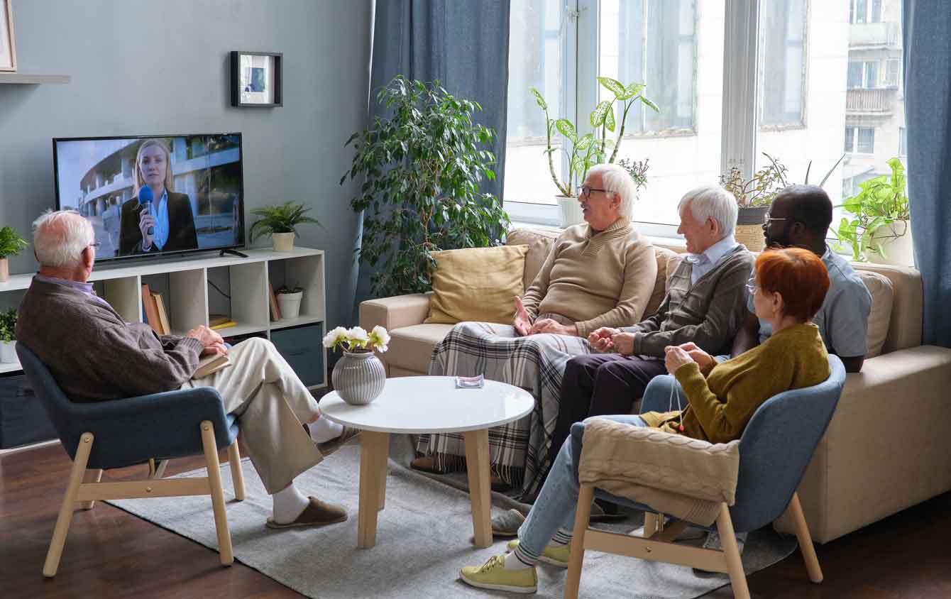 A group of seniors sit in a living room watching TV
