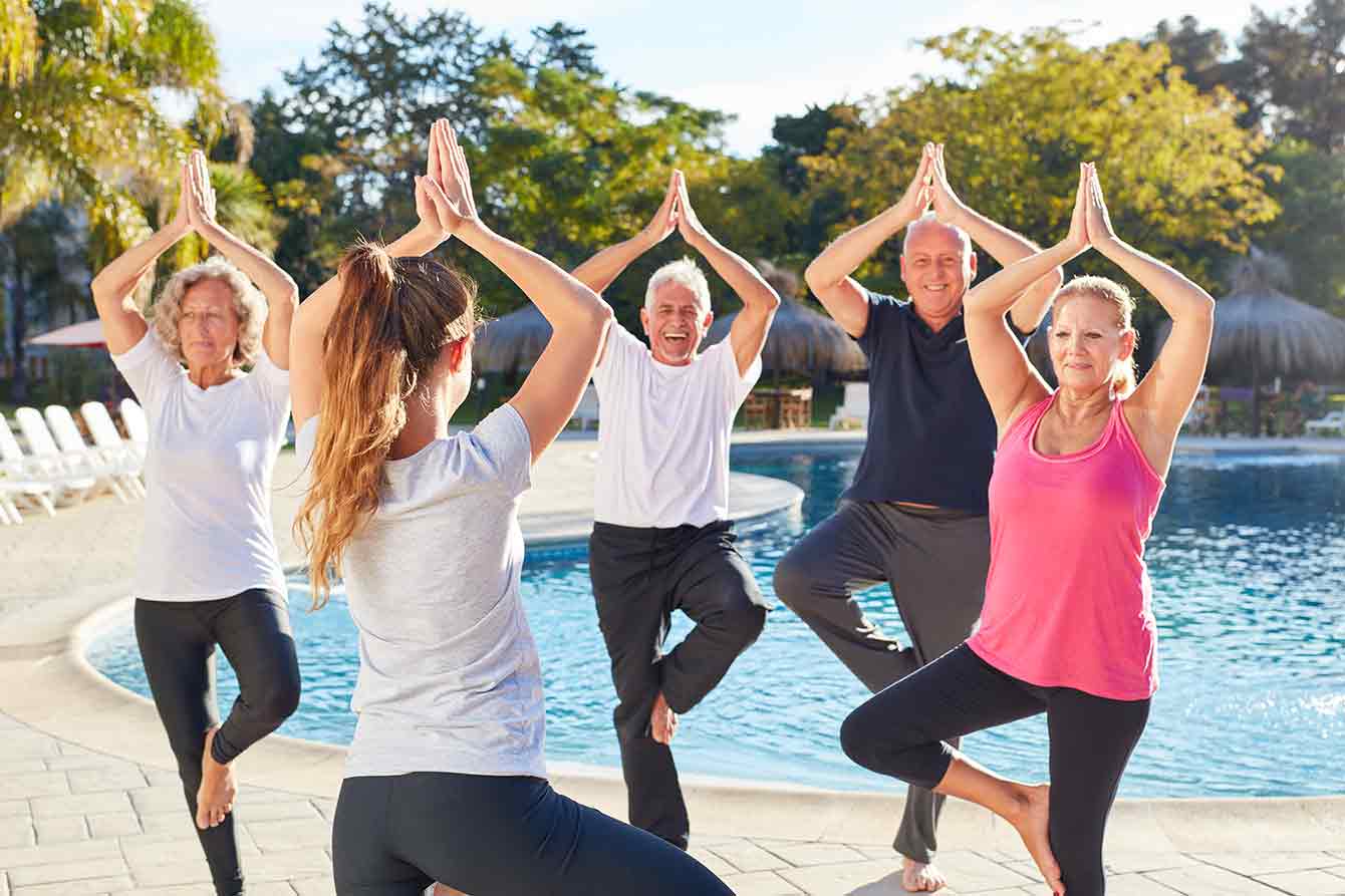 Group of seniors practice tree pose next to a pool