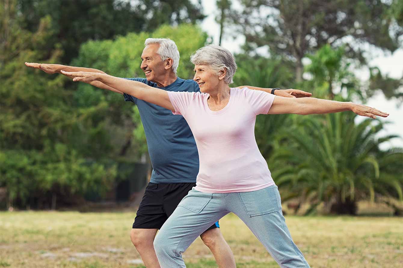 An older couple practice yoga in the park