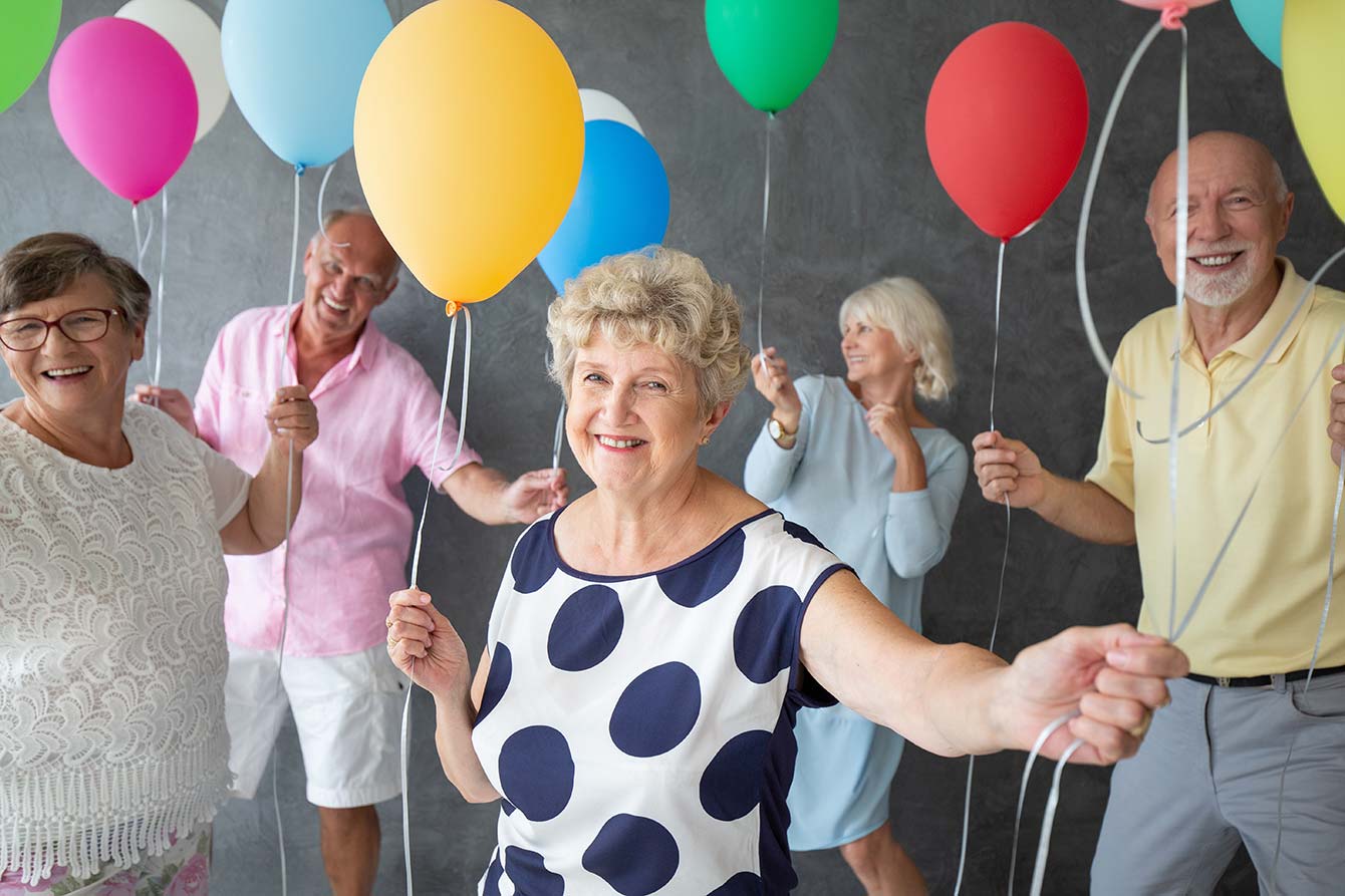 Smiling grandmother and happy friends with colorful balloons during party
