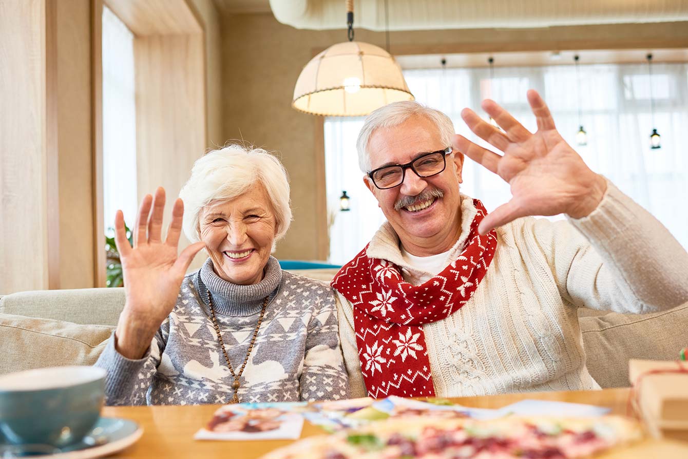Smiling senior couple looking at camera waving happily while enjoying dinner in cafe