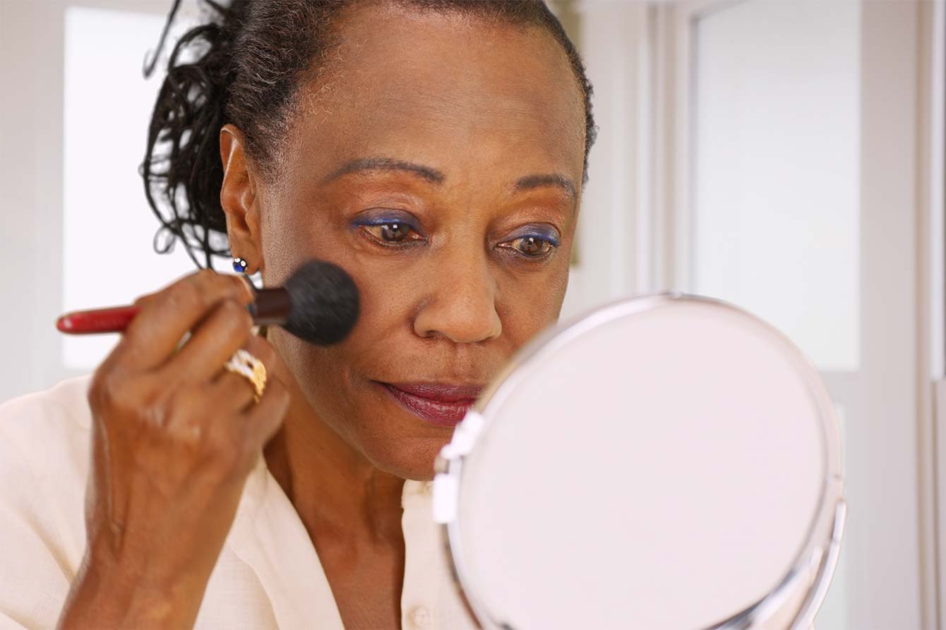 Pretty elderly black woman does her makeup in the mirror