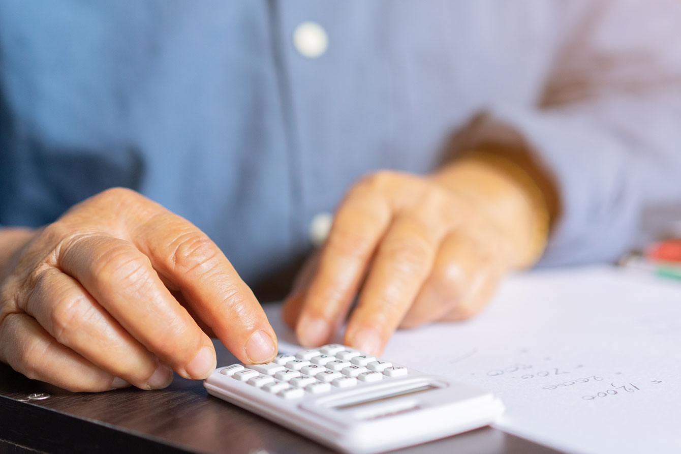 Senior putting numbers into a calculator next to notepad with calculations