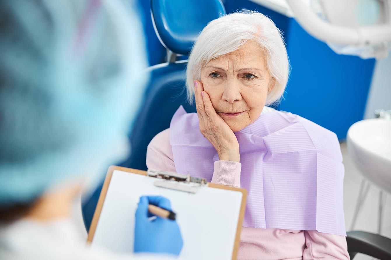 Older woman with tooth pain informs a dentist