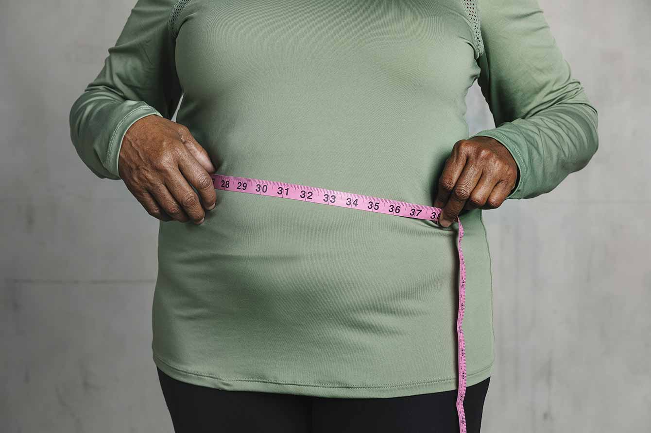 An older black woman measures her stomach with a tape measure