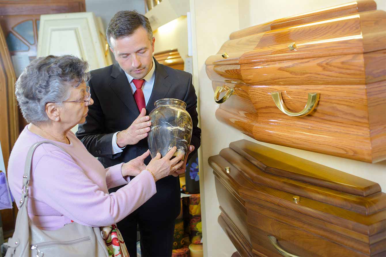 An elderly woman examines an urn in a funeral home assisted by a salesmen
