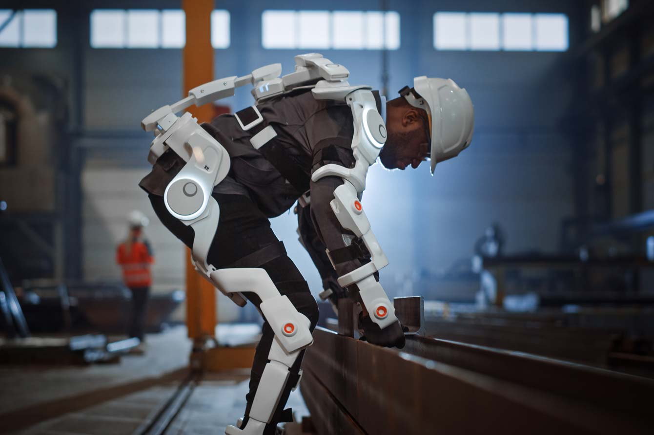 An african american man wearing an exoskeleton suit picks up a heavy metal objects