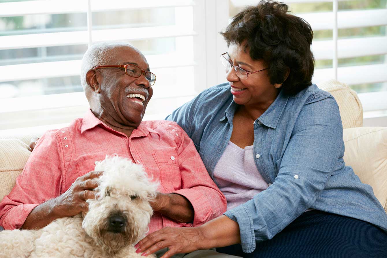 Happy black senior couple with dog on their sofa