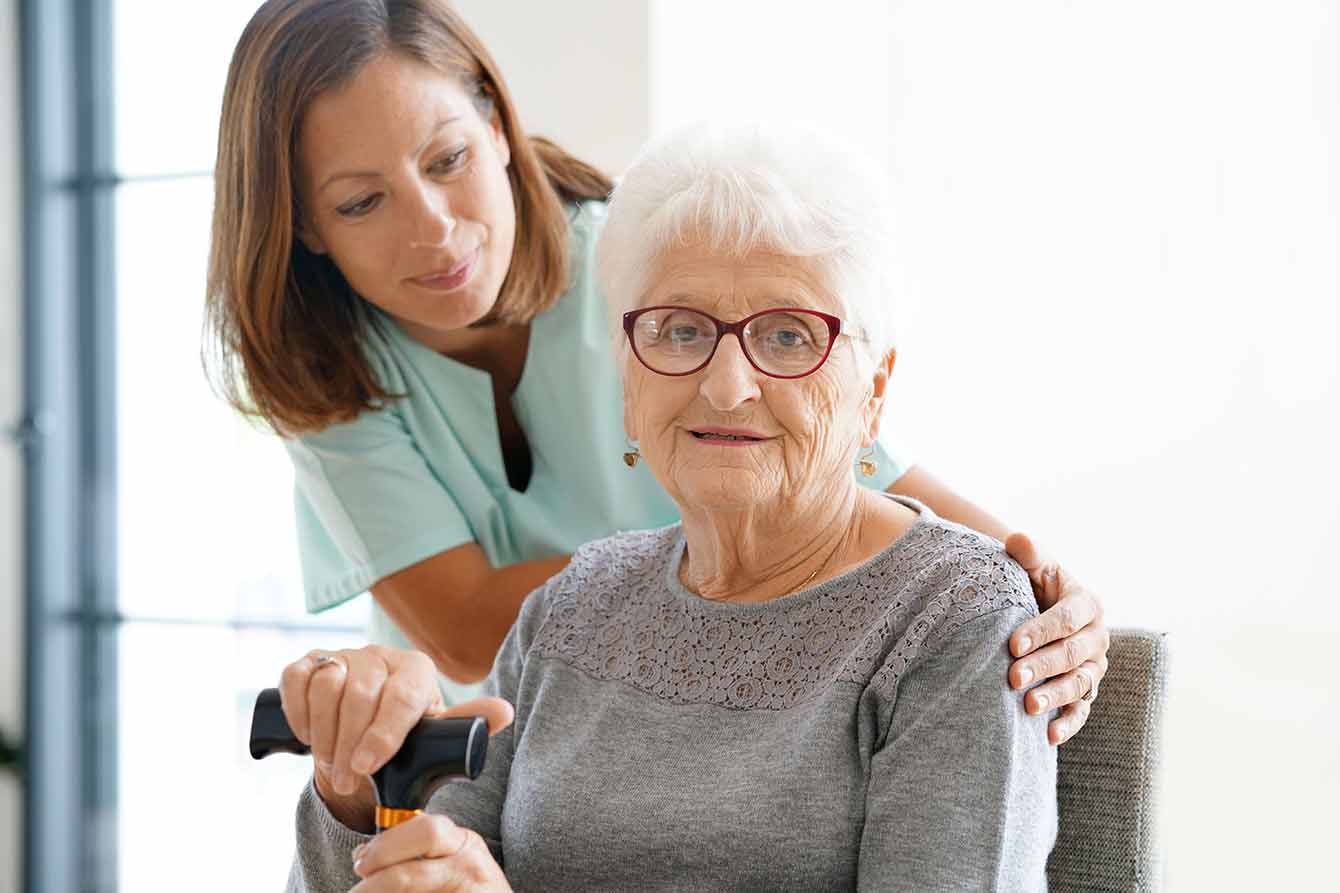 An attractive older woman with glasses and a cane is assisted by a younger woman