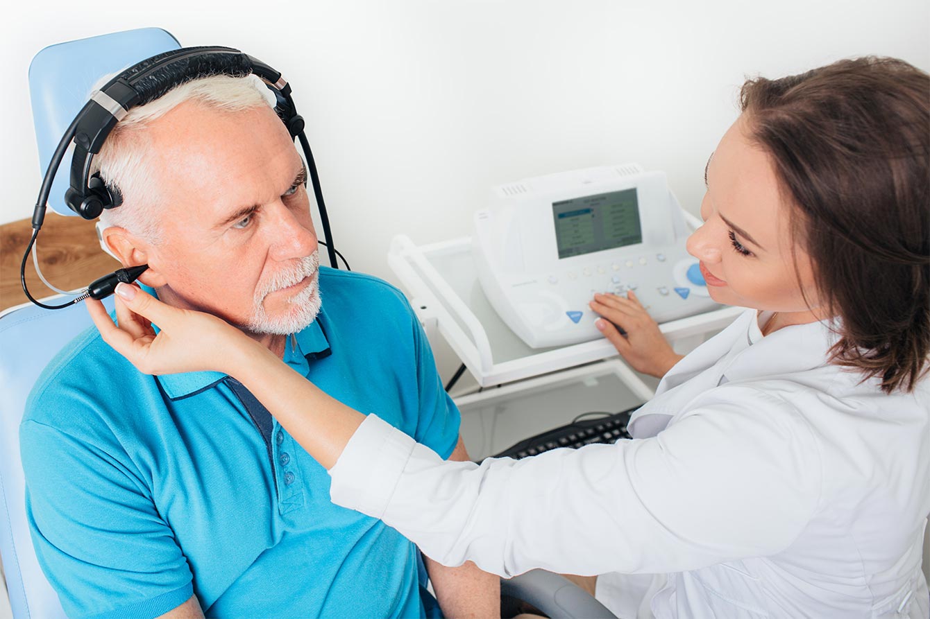 Senior man with blue shirt having ear examination with young female audiologist