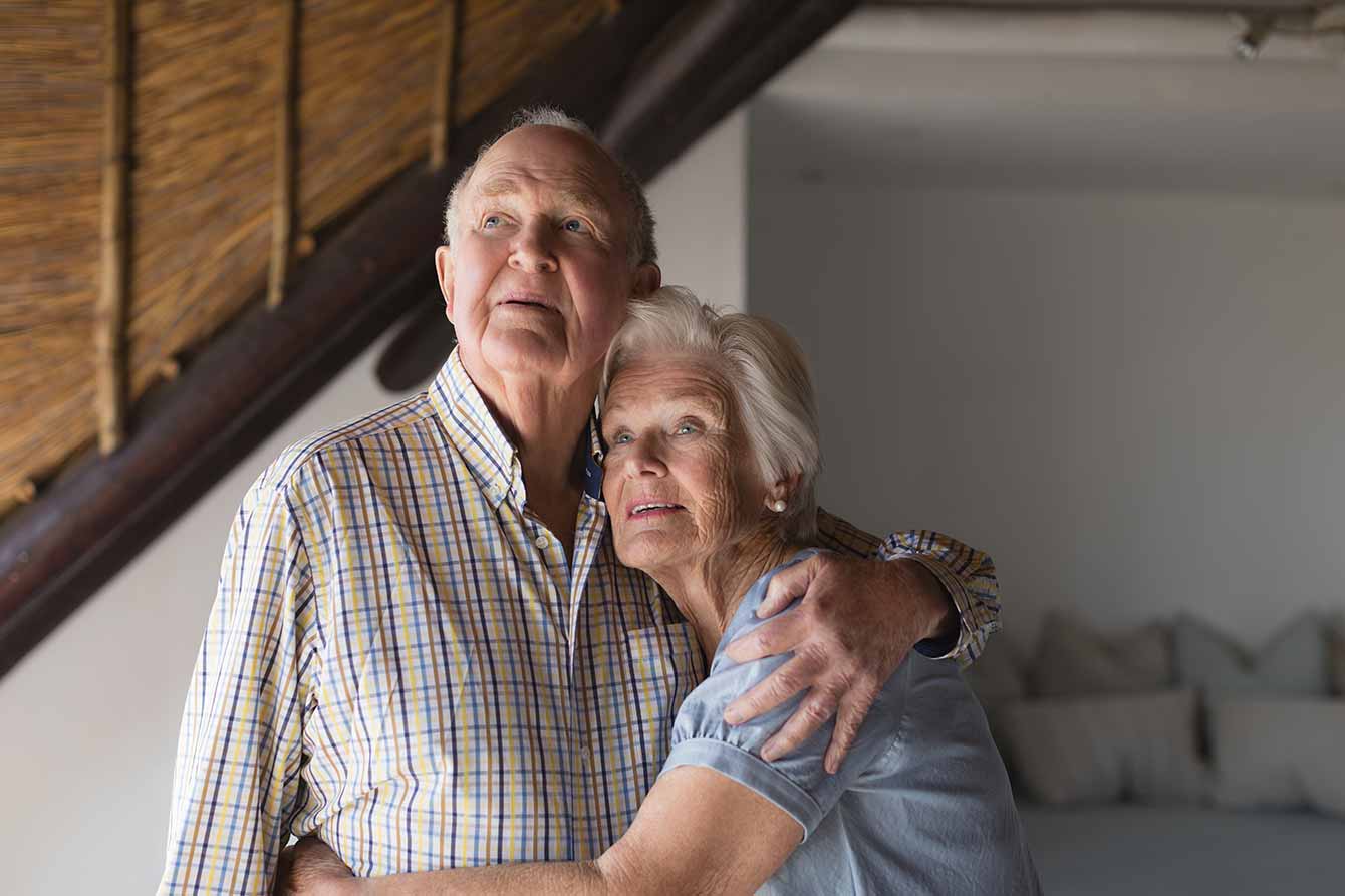 An older couple embrace inside of their home