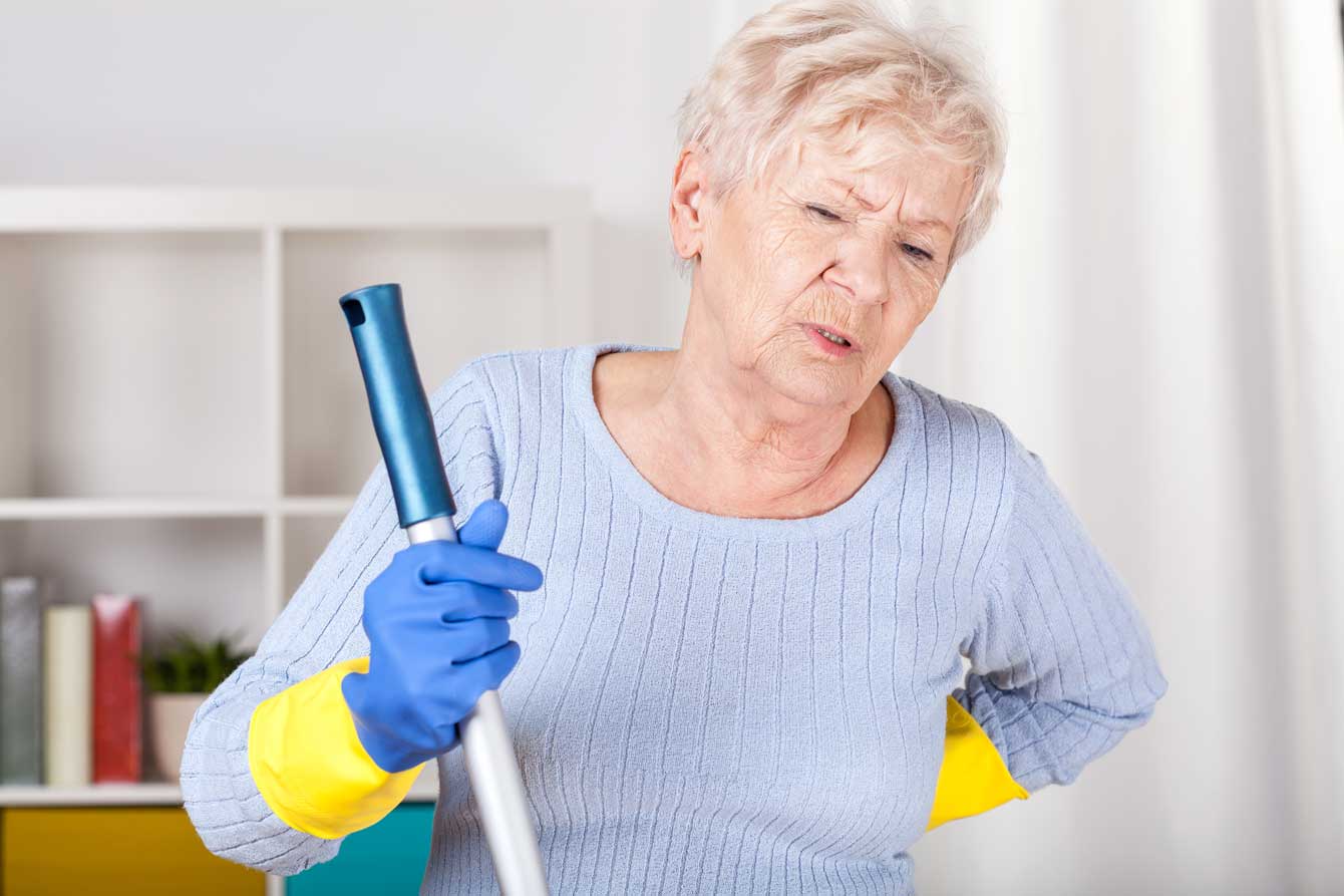 Older woman with mop has a pained expression, hand on her back