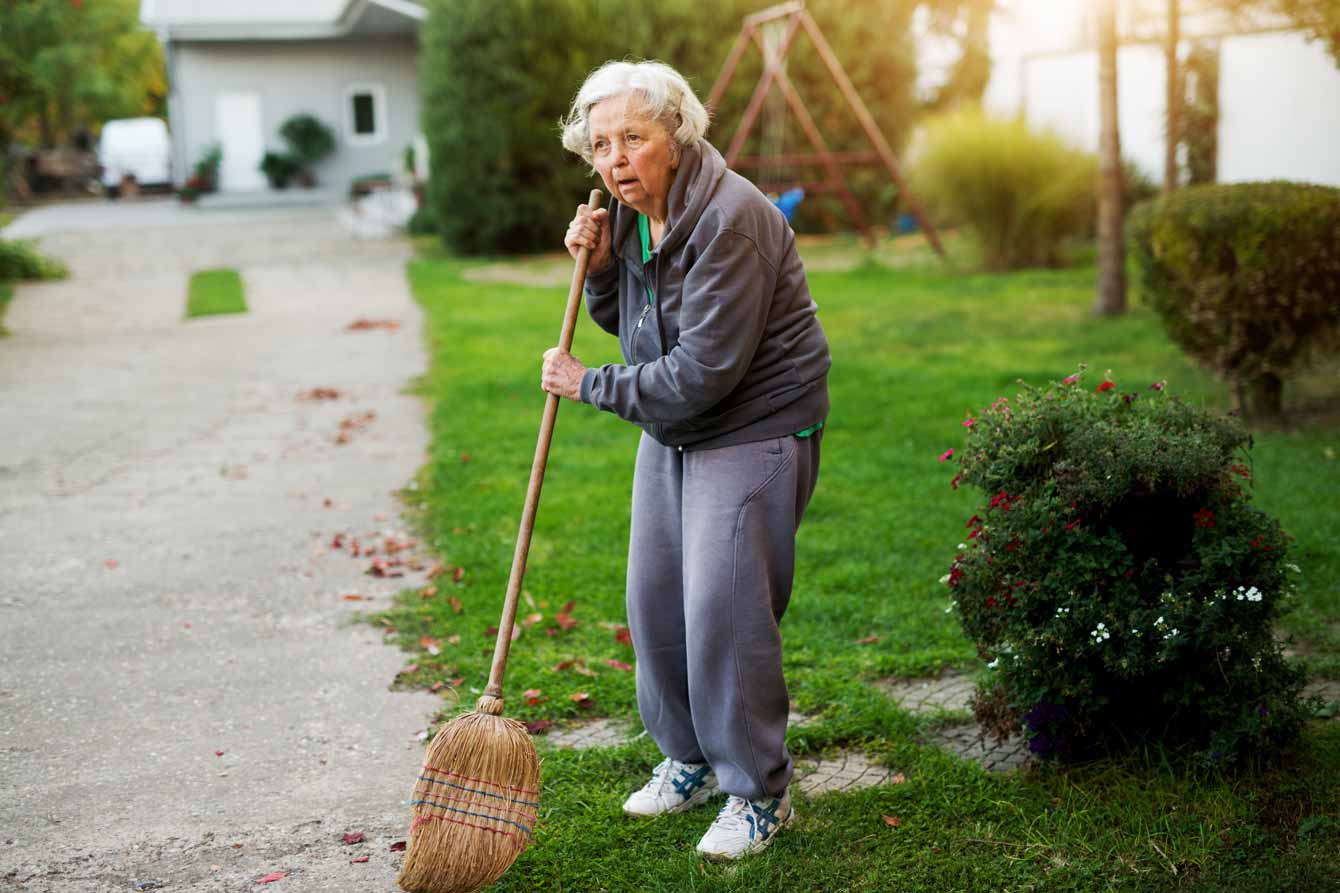Tired senior woman holding broom in her backyard