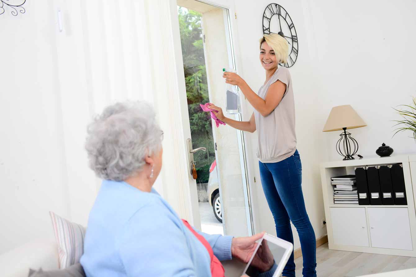 Smiling young woman helps an older senior woman with household chores