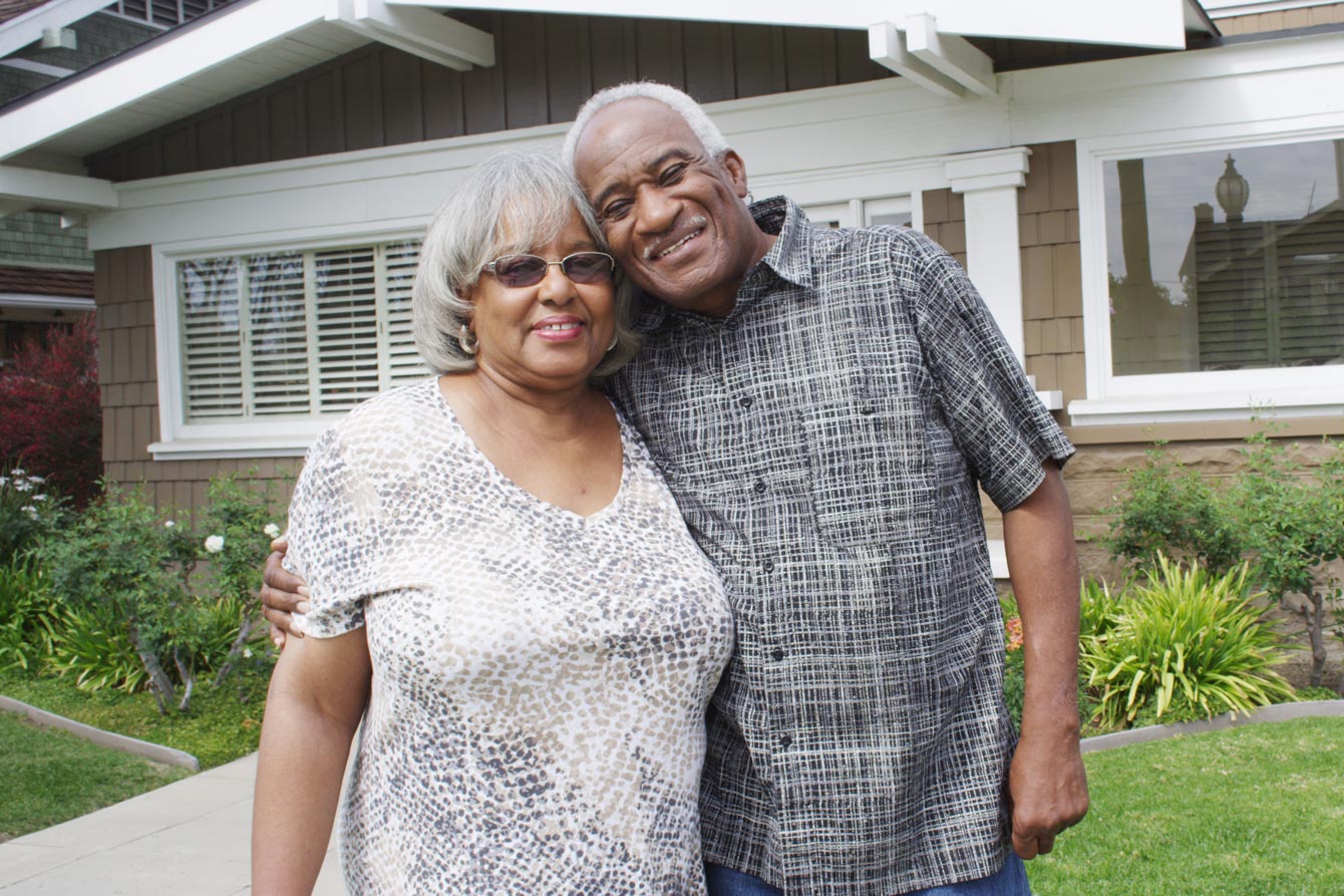 African American senior couple stand happily in front of their houser
