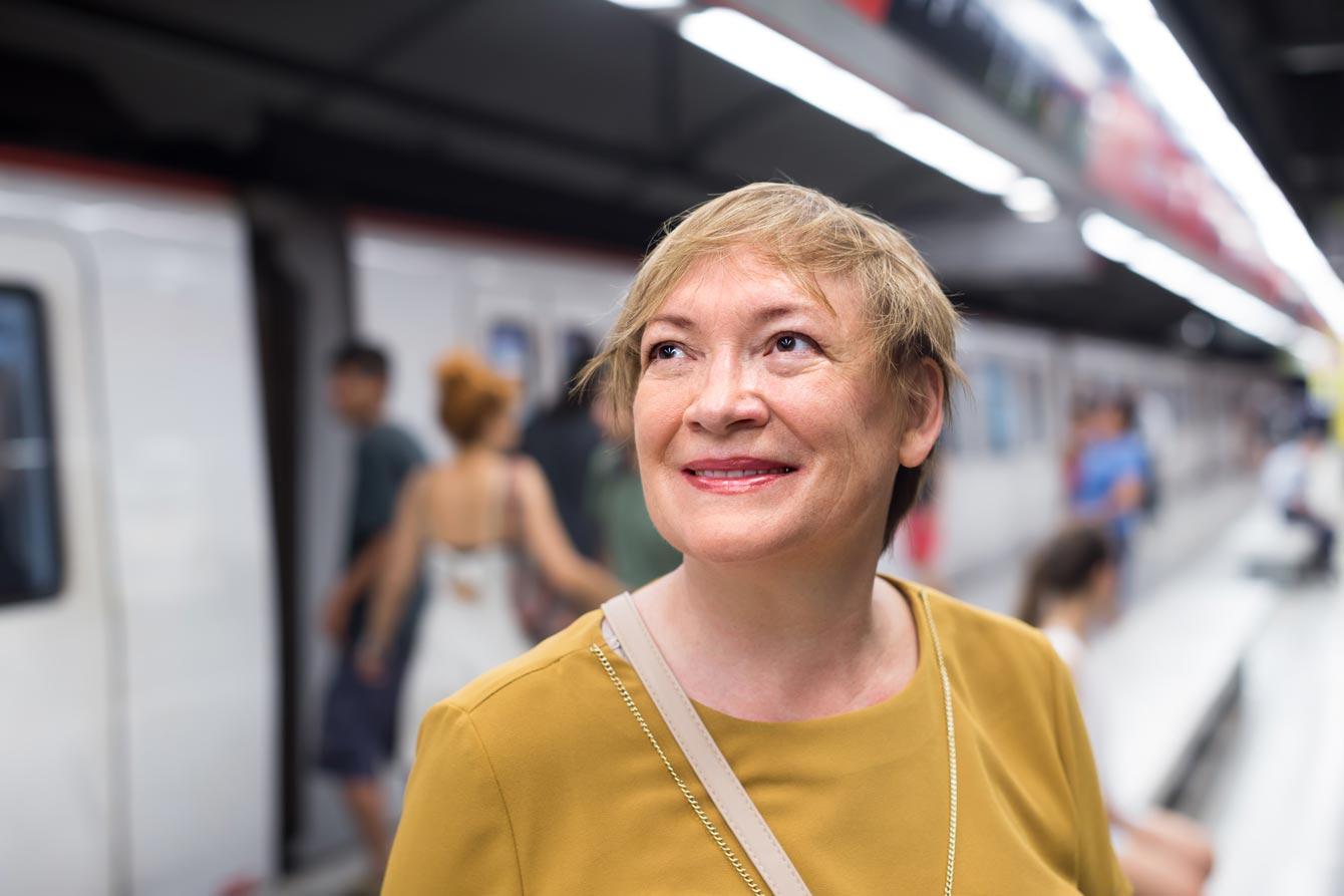 An older woman stands in front of a subway train