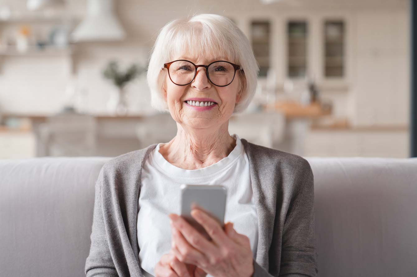 Smiling older woman sits on couch holding cell phone