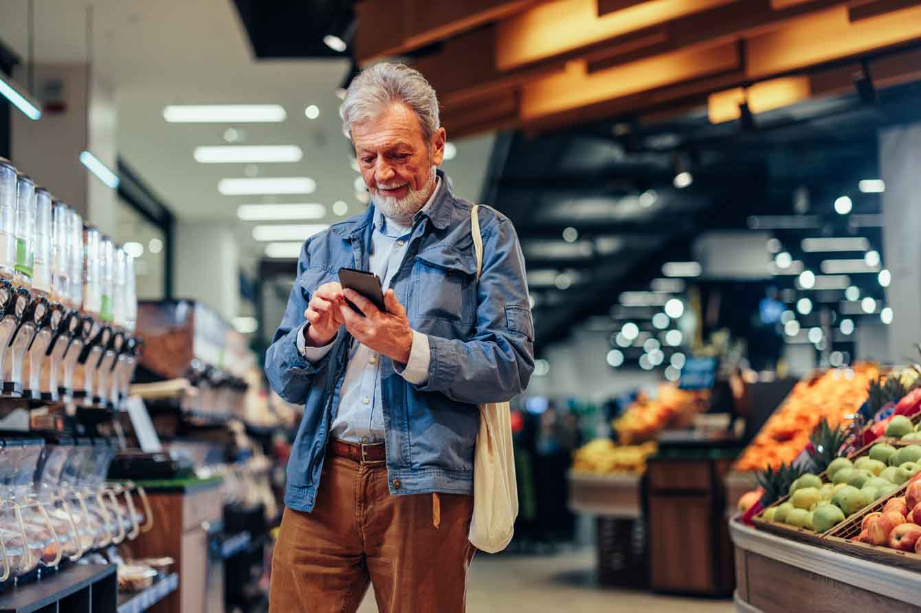 Mature man looks at cell phone while shopping in grocery store