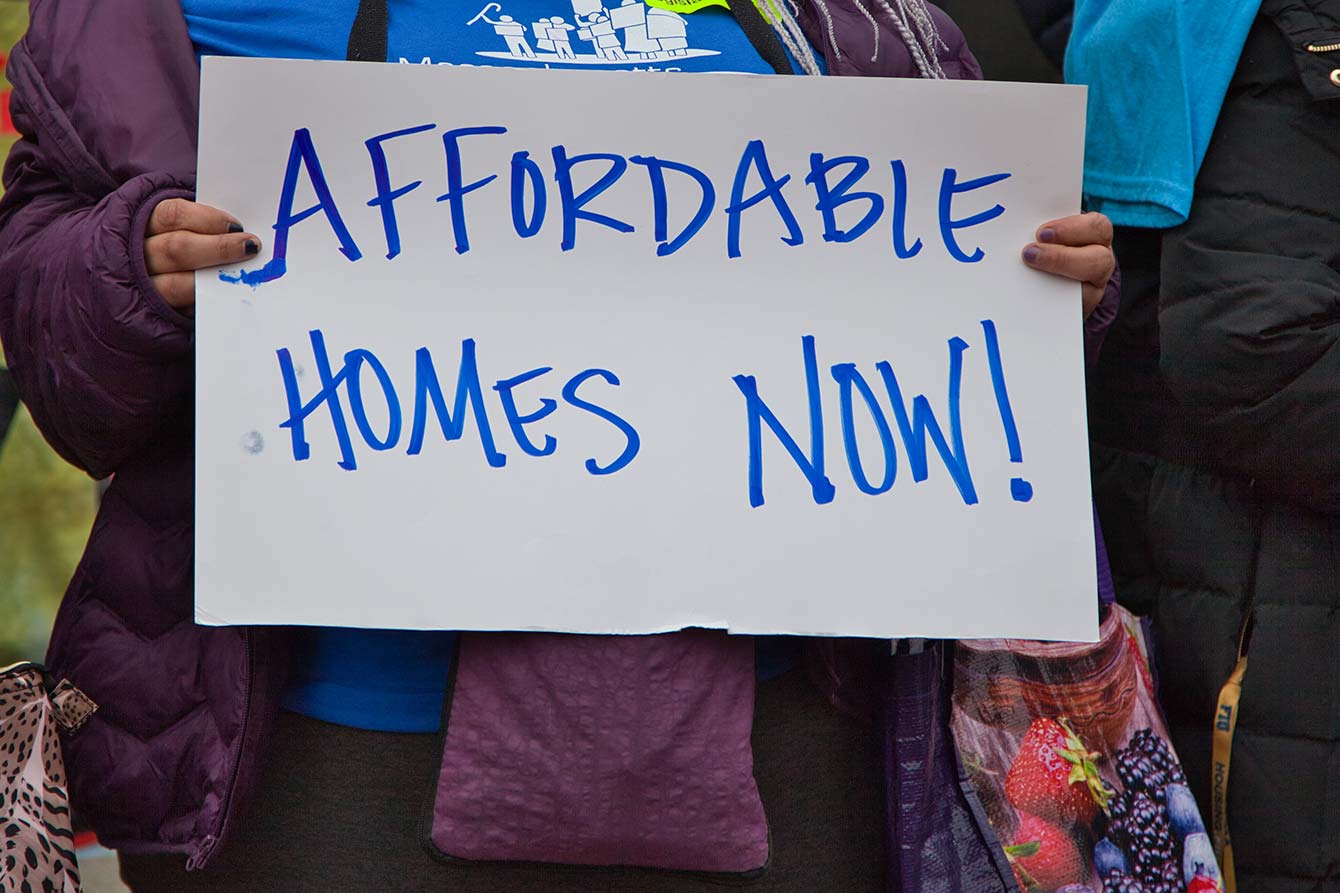 A woman holds a sign that reads Affordable Housing Now