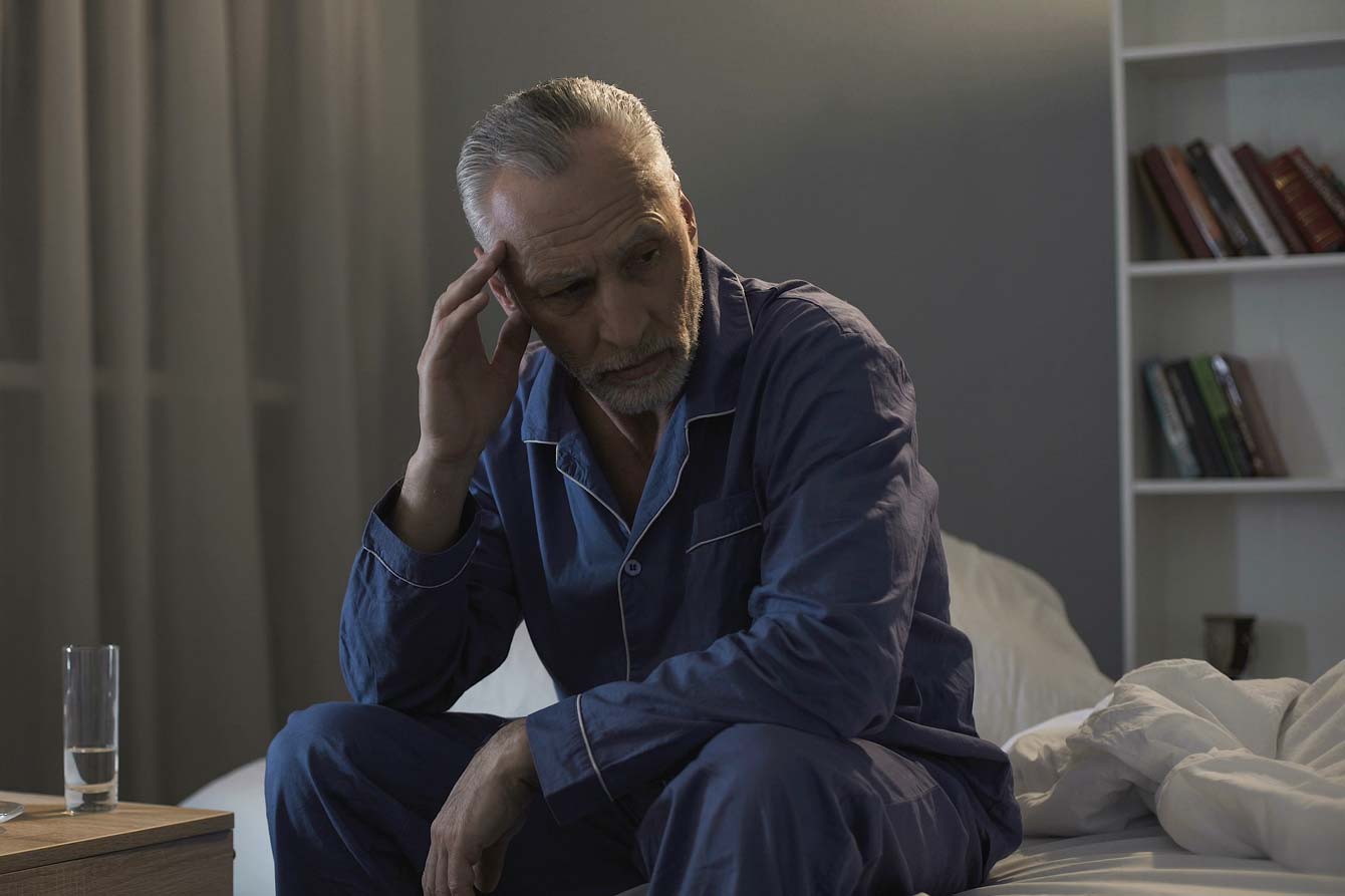 A senior man sits on his bed unable to sleep at night