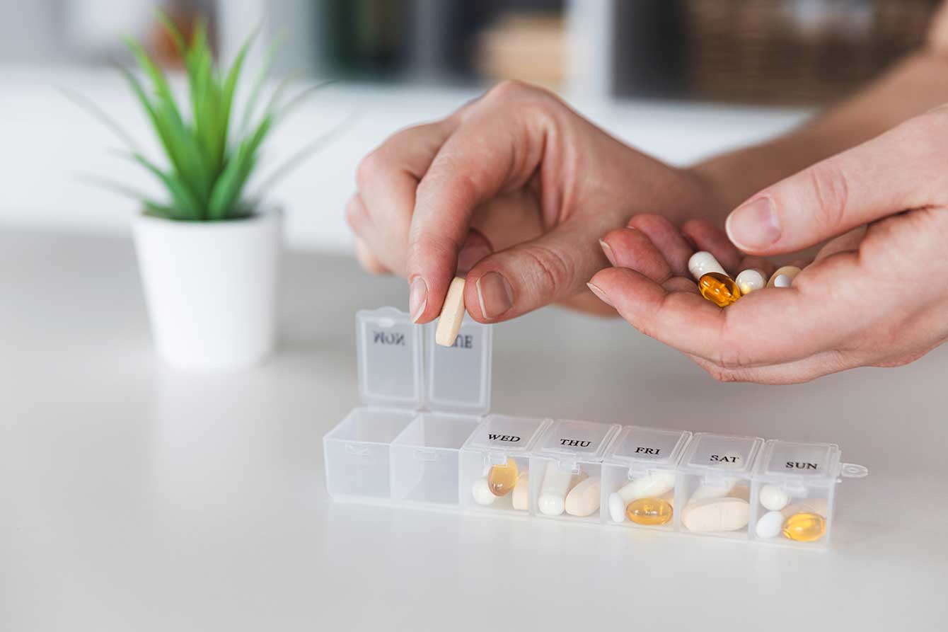 Elderly women's hands putting supplements into a plastic container