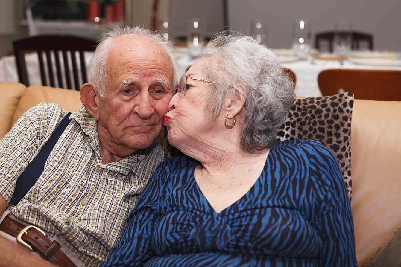 An older lady kisses her husband's cheek