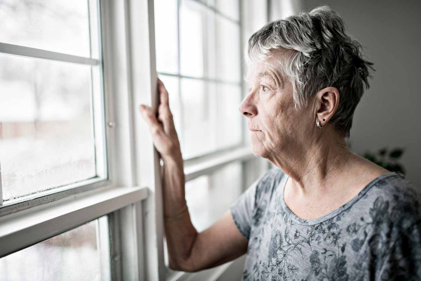 A sad and lonely elderly woman looks out her window