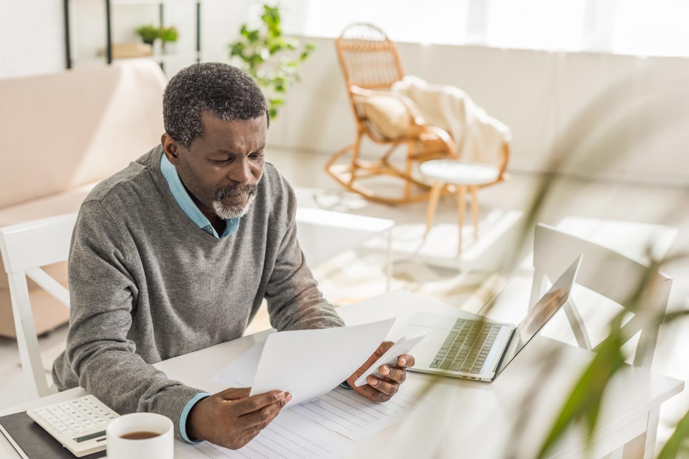 Senior African American man looking at documents while sitting at desk near laptop