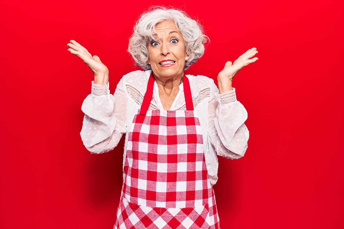 Senior grey-haired woman wearing apron confused with open arms